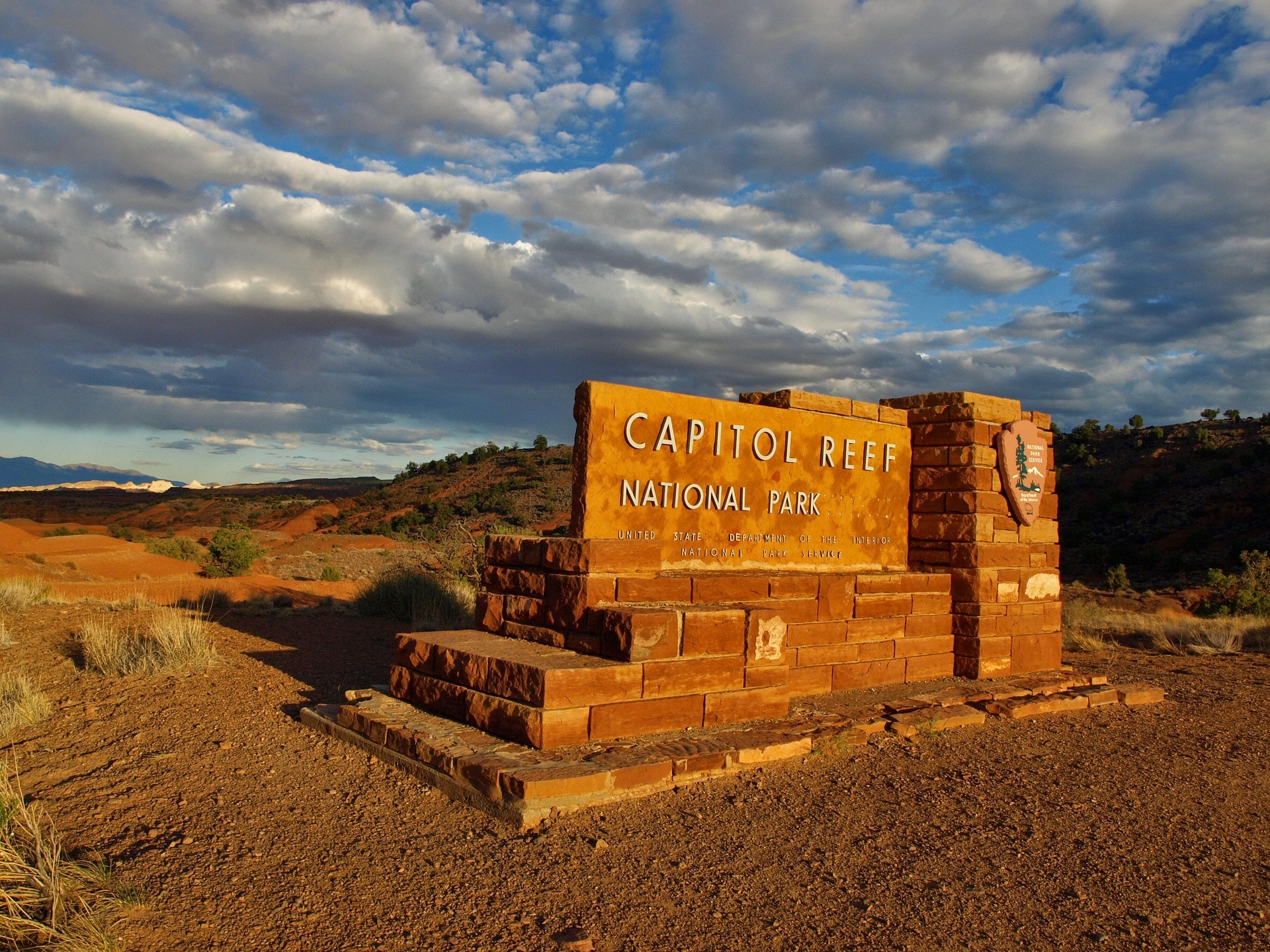 Capitol Reef National Park entrance sign built from red sandstone blocks under a dramatic sunset sky