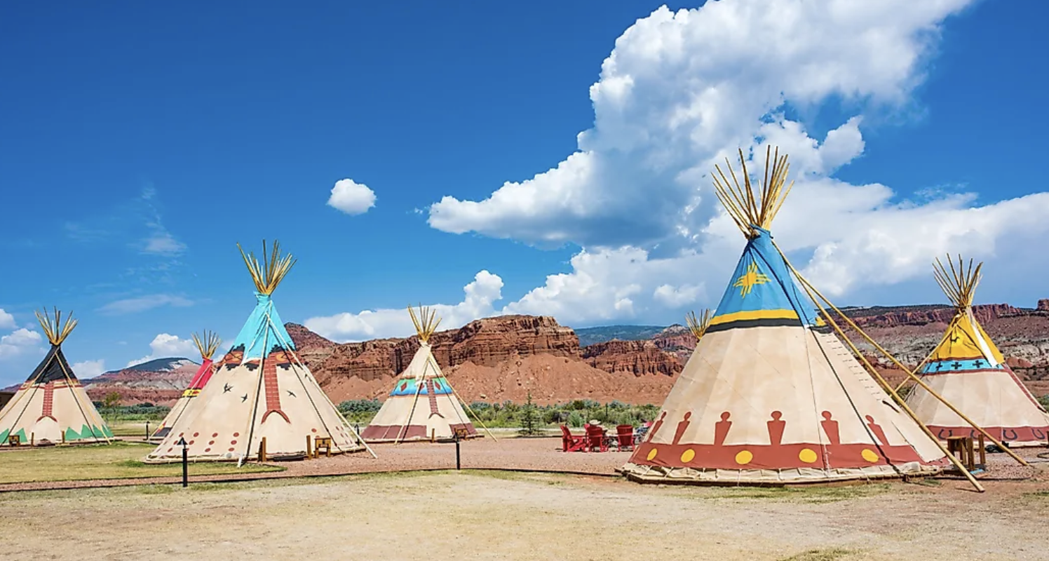 A row of painted teepees at Capitol Reef Resort with red cliffs behind in Torrey, Utah