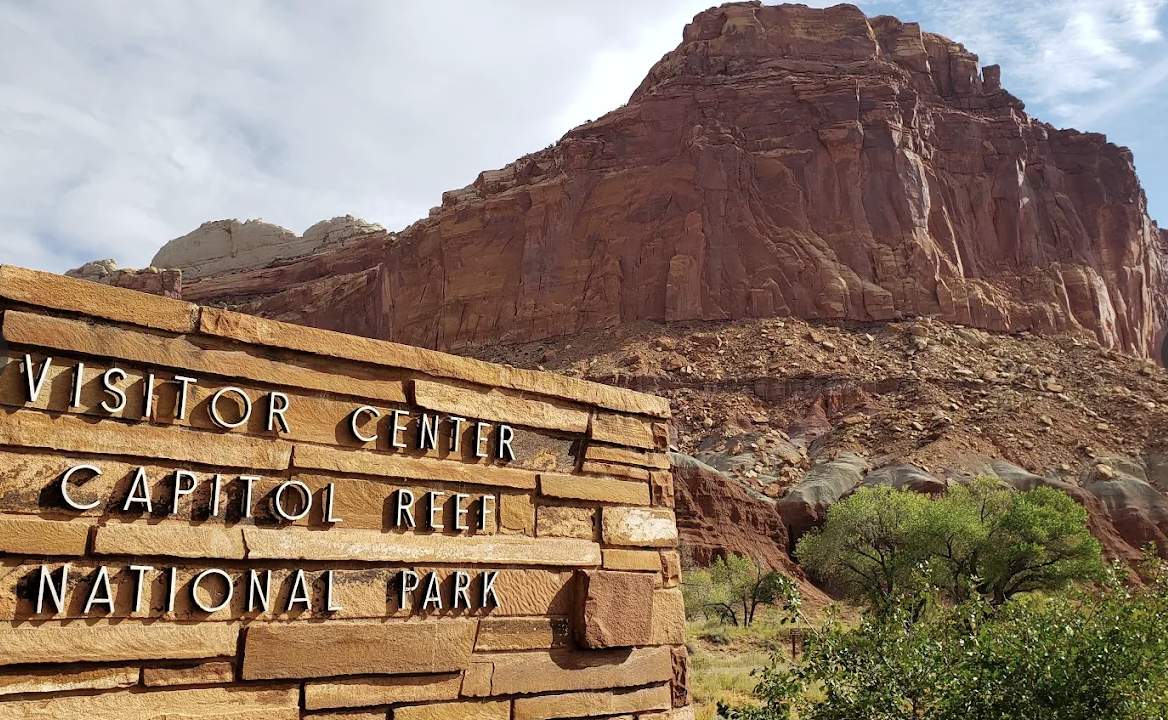 The stone Visitor Center sign for Capitol Reef National Park with the Castle formation rising behind it