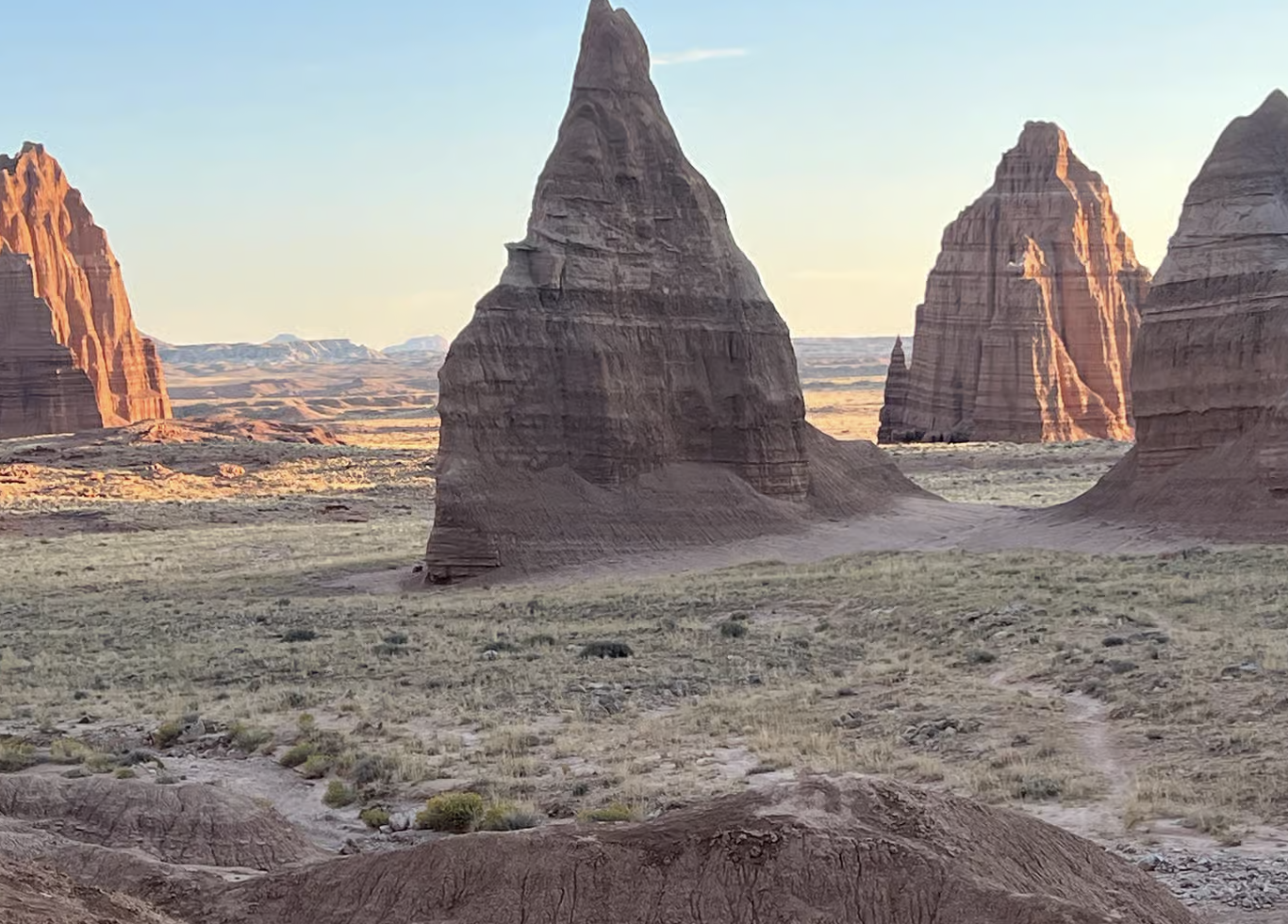 Tall red rock monoliths rising from a grassy valley floor at golden hour in Cathedral Valley, Capitol Reef National Park