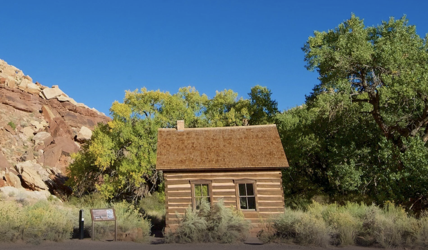 The log Fruita Schoolhouse with a National Park Service interpretive sign in Capitol Reef National Park