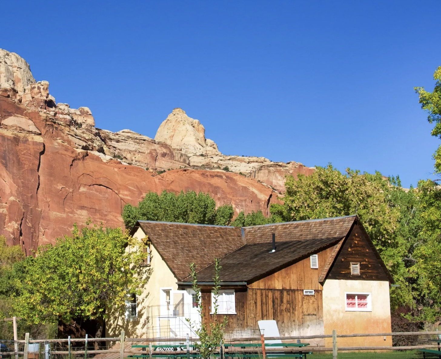 A cream and brown farmhouse below layered red and white cliffs in the Fruita Historic District, Capitol Reef National Park