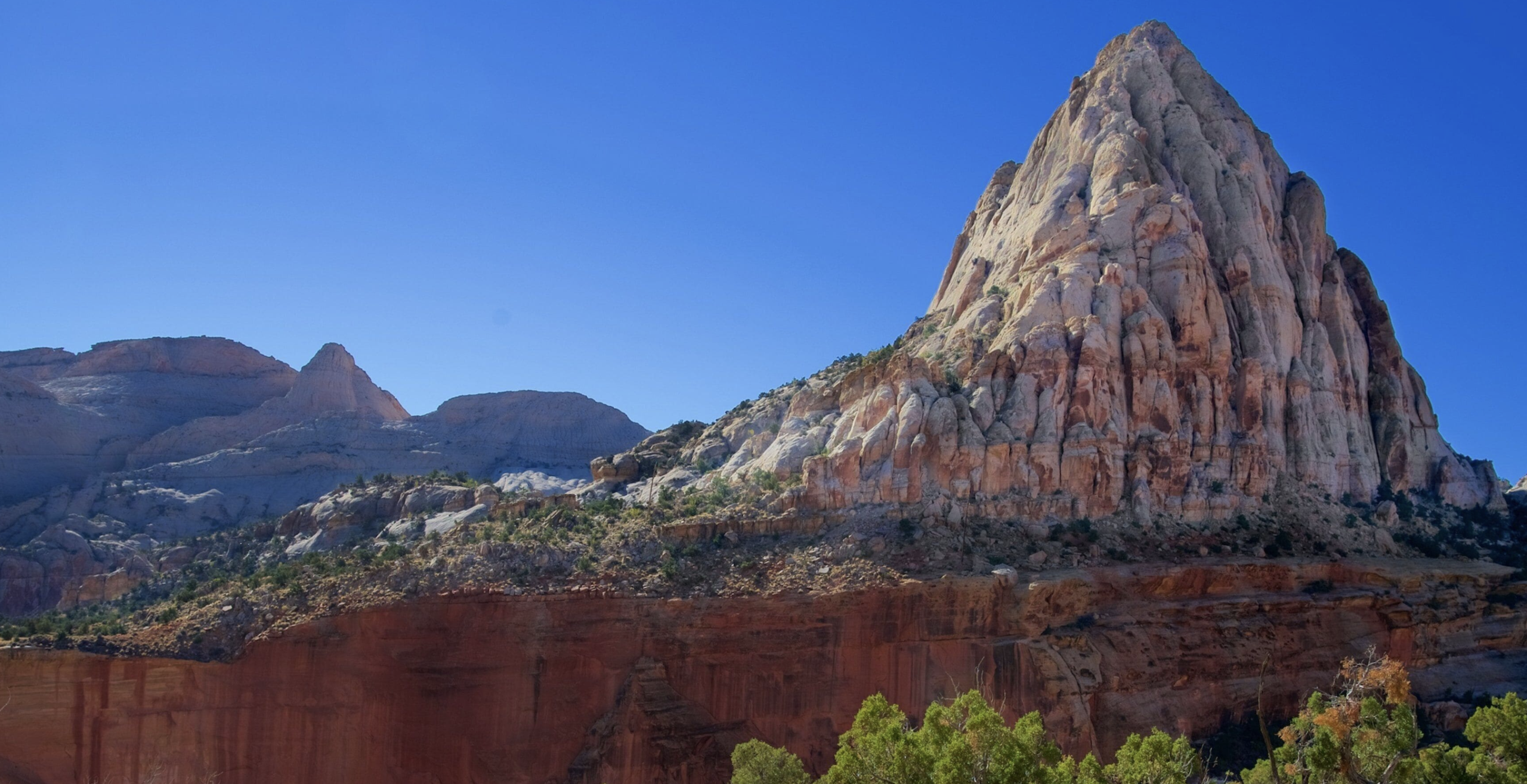 A tall triangular white and tan sandstone peak resembling Golden Throne rising above the reef's cliffs in Capitol Reef National Park