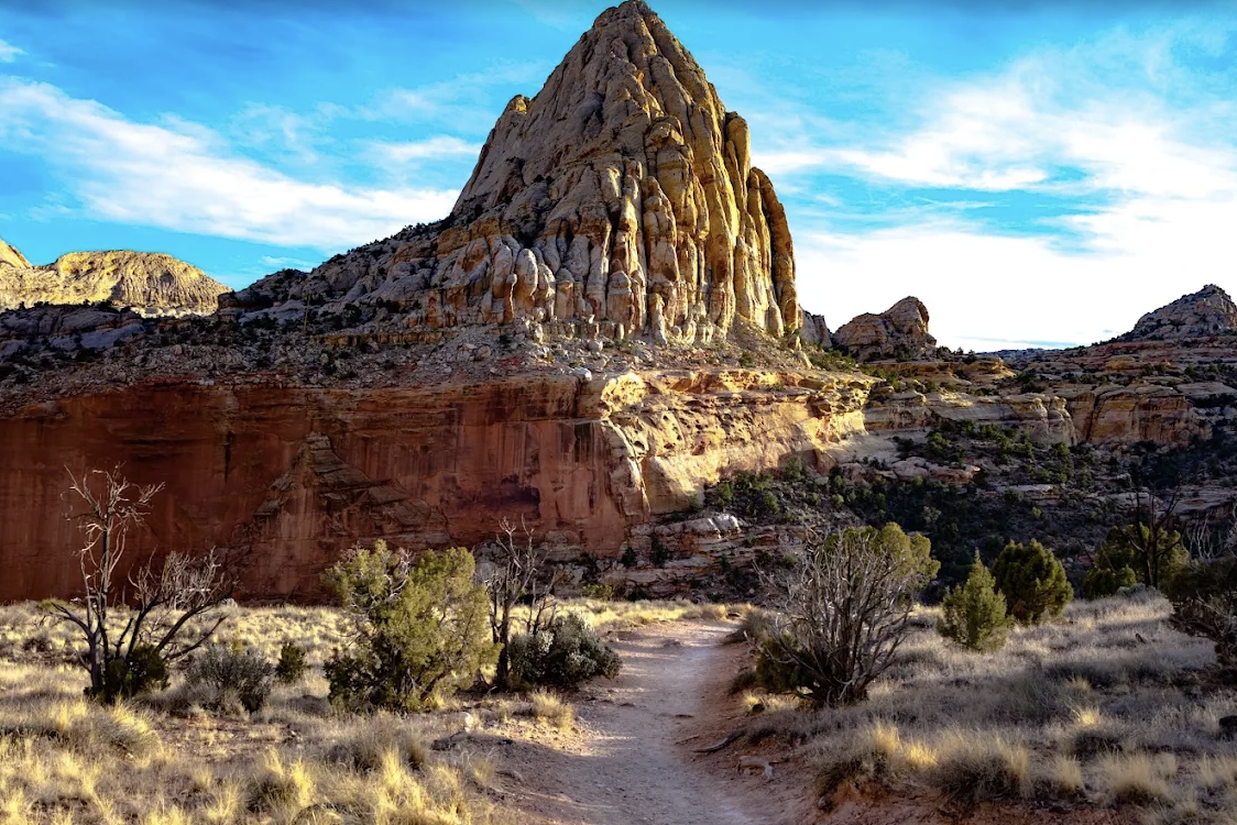 A tall triangular sandstone peak resembling Golden Throne seen from a hiking trail in Capitol Reef National Park