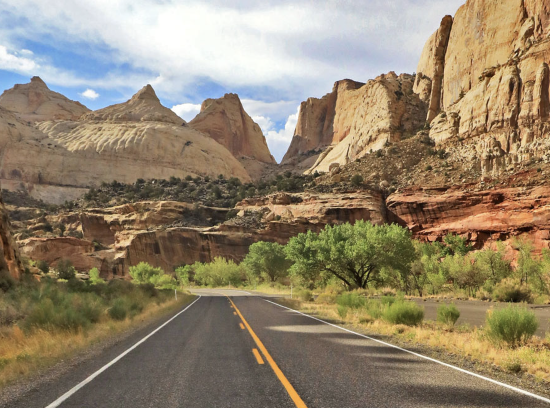 A two lane highway running below tall sandstone spires and cliffs in Capitol Reef National Park