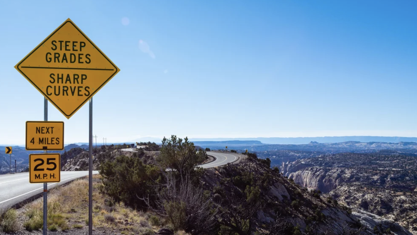 A steep grades and sharp curves warning sign above the narrow Hogback ridge on Scenic Byway 12