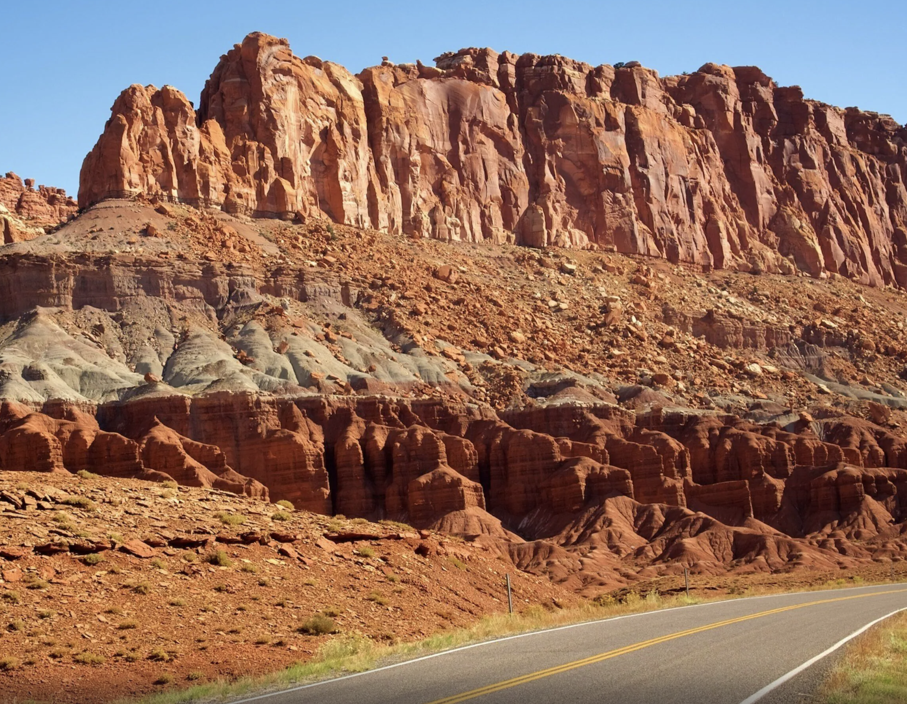 Banded red and gray cliffs rising above a two lane road in Capitol Reef National Park