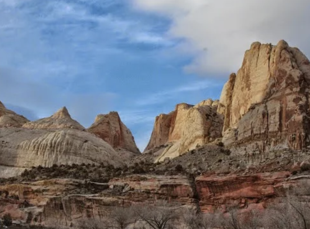 Cream colored sandstone domes and red rock cliffs under a partly cloudy sky in Capitol Reef National Park