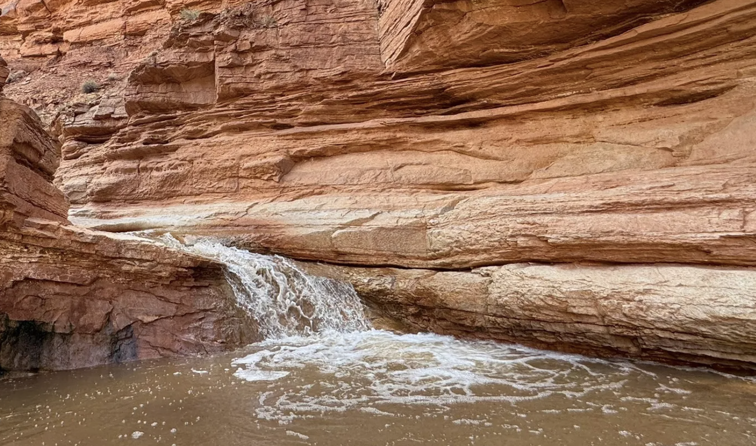 A small waterfall pouring over a sandstone ledge into a canyon stream in Capitol Reef country, Utah