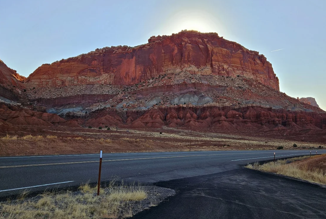 The sun rising behind a large red rock butte above a highway near Capitol Reef National Park