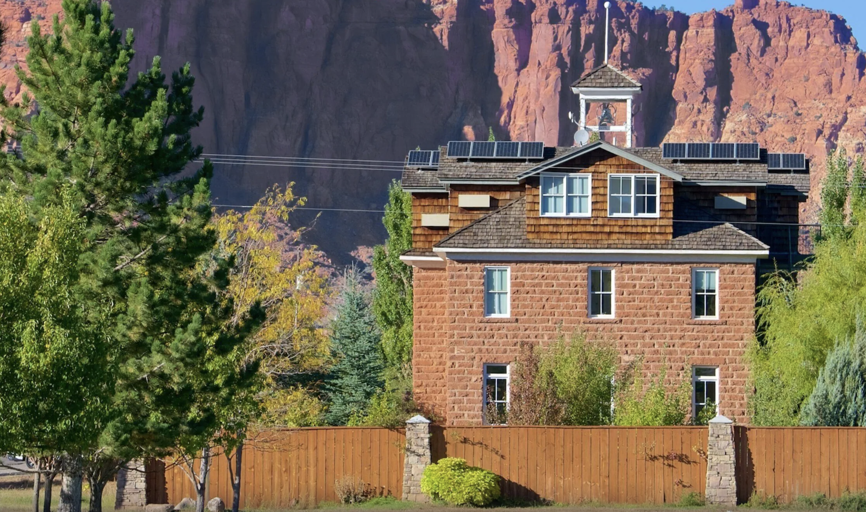 A brick schoolhouse building with a bell cupola and solar panels, home to the Torrey Schoolhouse Bed and Breakfast in Torrey, Utah