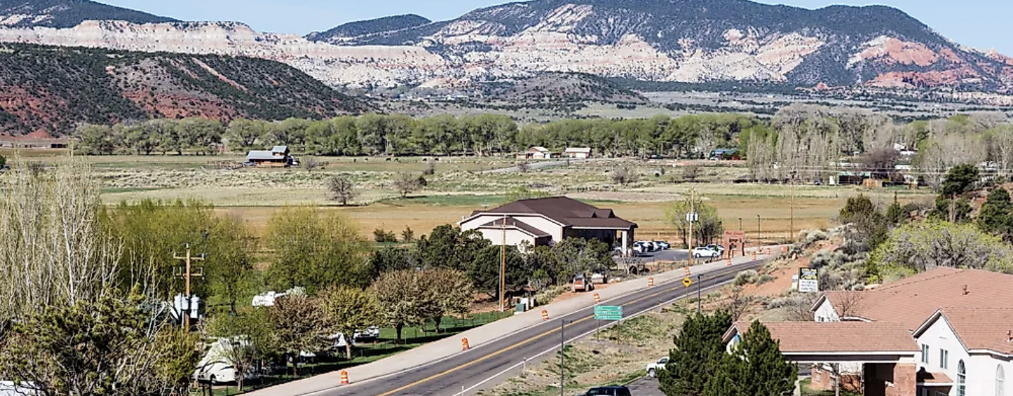 An elevated view of a small Utah town with fields, a two lane highway, and a high plateau rising behind