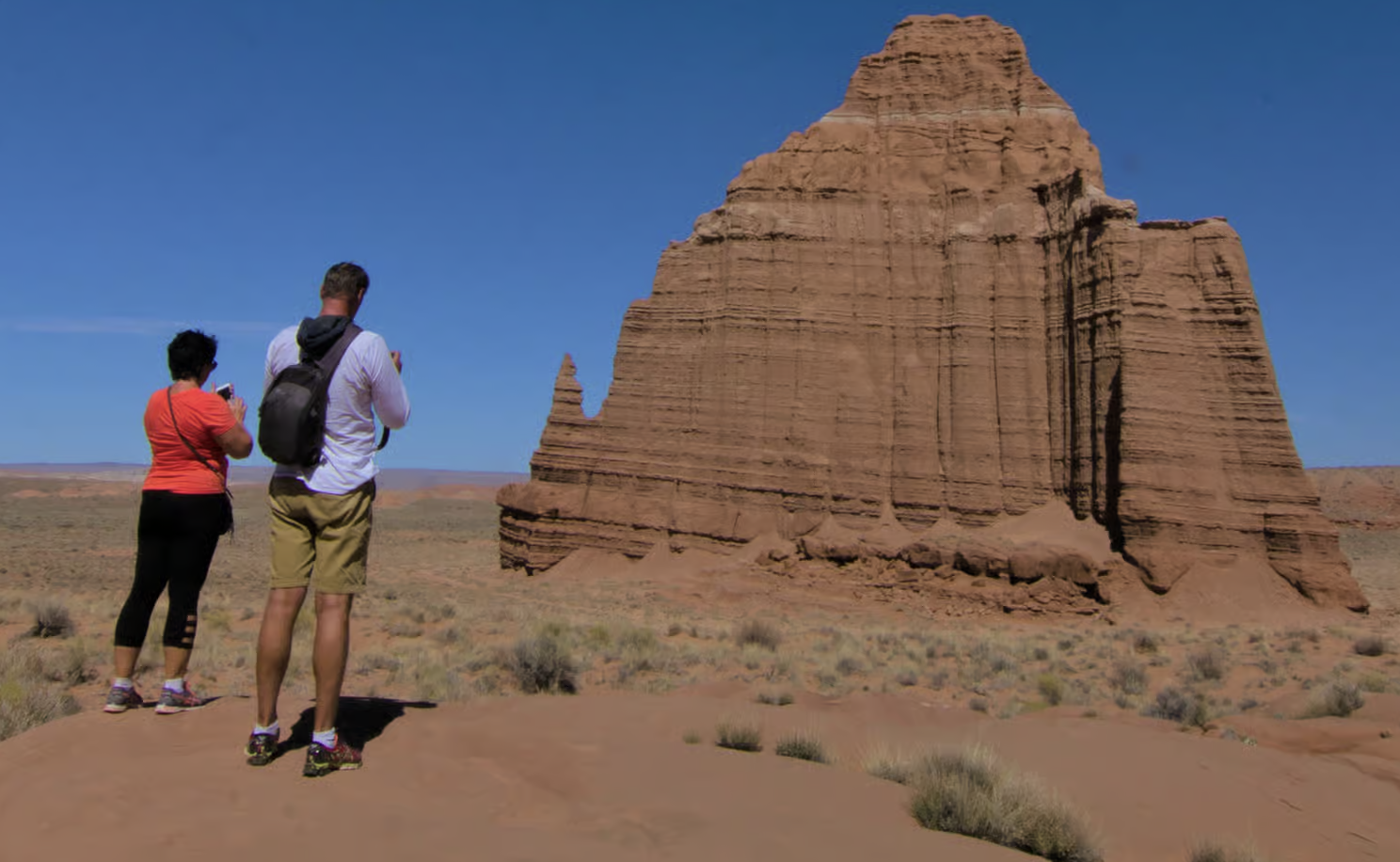 Two tourists photographing a tall banded sandstone monolith in Cathedral Valley, Capitol Reef National Park